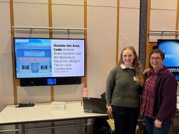 Margaret Christoffersen standing by Sheila Murphy and her project, "Outside of the Area Code: Bulletin Board Systems’ and the Blacksburg Electronic Village’s Ties to Local Communities."